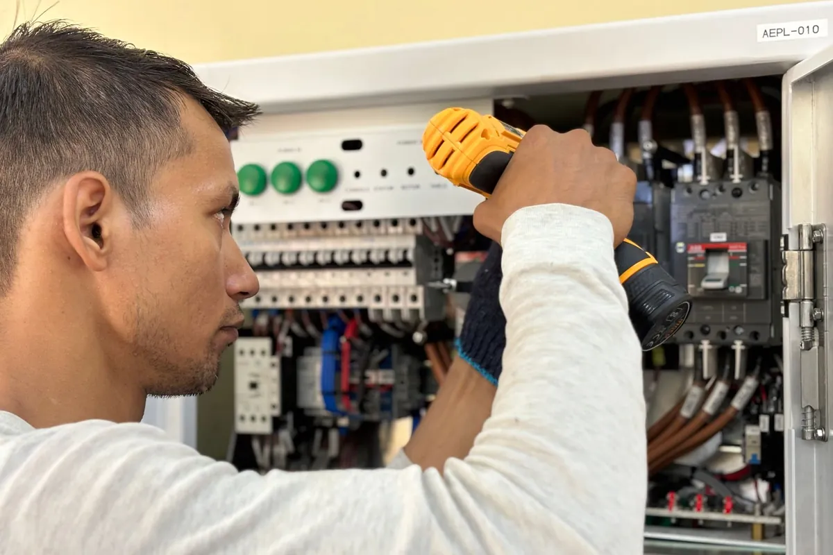 Electrician using a power drill to fit an indoor circuit breaker panel, the daily electrical work electrician software is built to organise