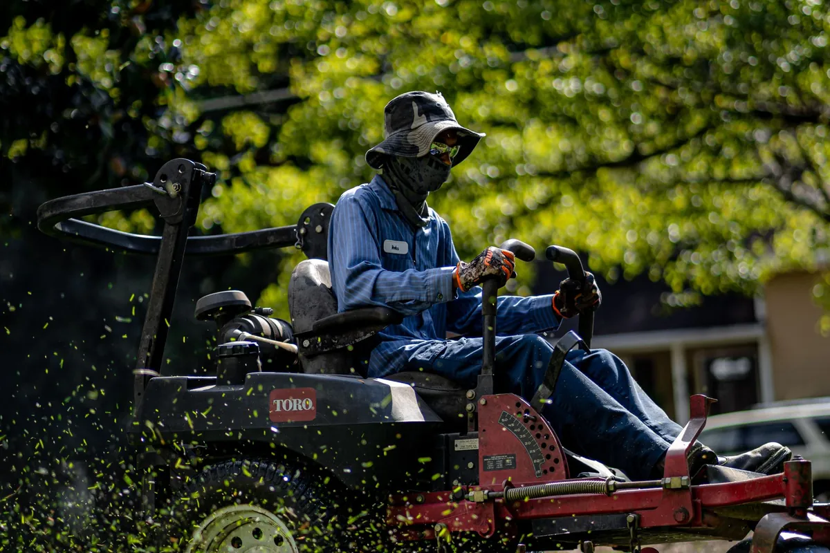 Landscaping professional riding a commercial mower across a sunny green lawn, cutting grass on a regular lawn care service route